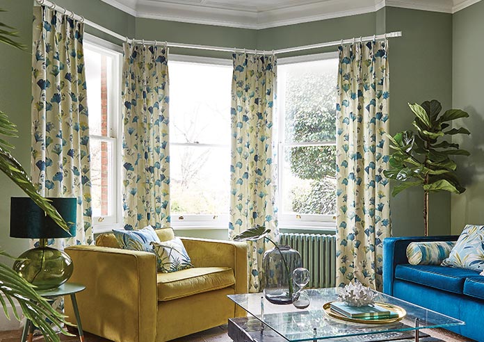 Floral green and blue curtains adorn a bay window in a green living room.