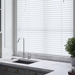 A white faux wooden blind adorns a window in a kitchen. A small plant is on the right of a marbled, grey-toned sink area.