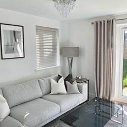 An image showing a living room with a wooden blind in a side window and eyelet curtains covering the french doors