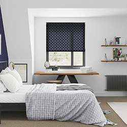 A blue and gold patterned roller blind in a minimalistic bedroom