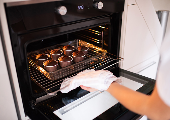 An image of a woman taking out buns from the oven