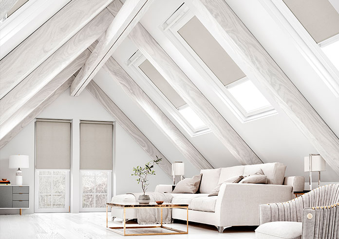 A select of grey blackout roller blinds show in a neutral white living room attic space.