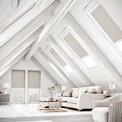 A select of grey blackout roller blinds show in a neutral white living room attic space.