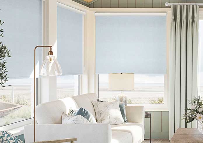 An image showing a beach front living room with wide windows adorned with blue roller blinds