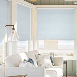 An image showing a beach front living room with wide windows adorned with blue roller blinds